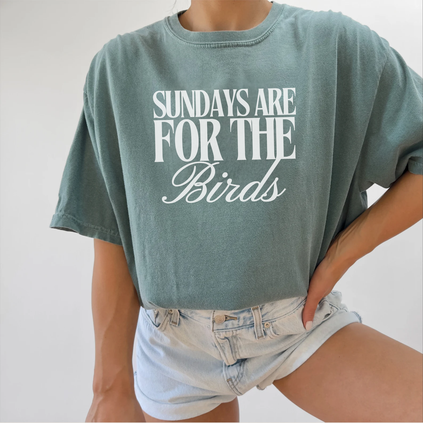 Person wearing a green t-shirt with 'Sundays are for the Birds' text on a plain background