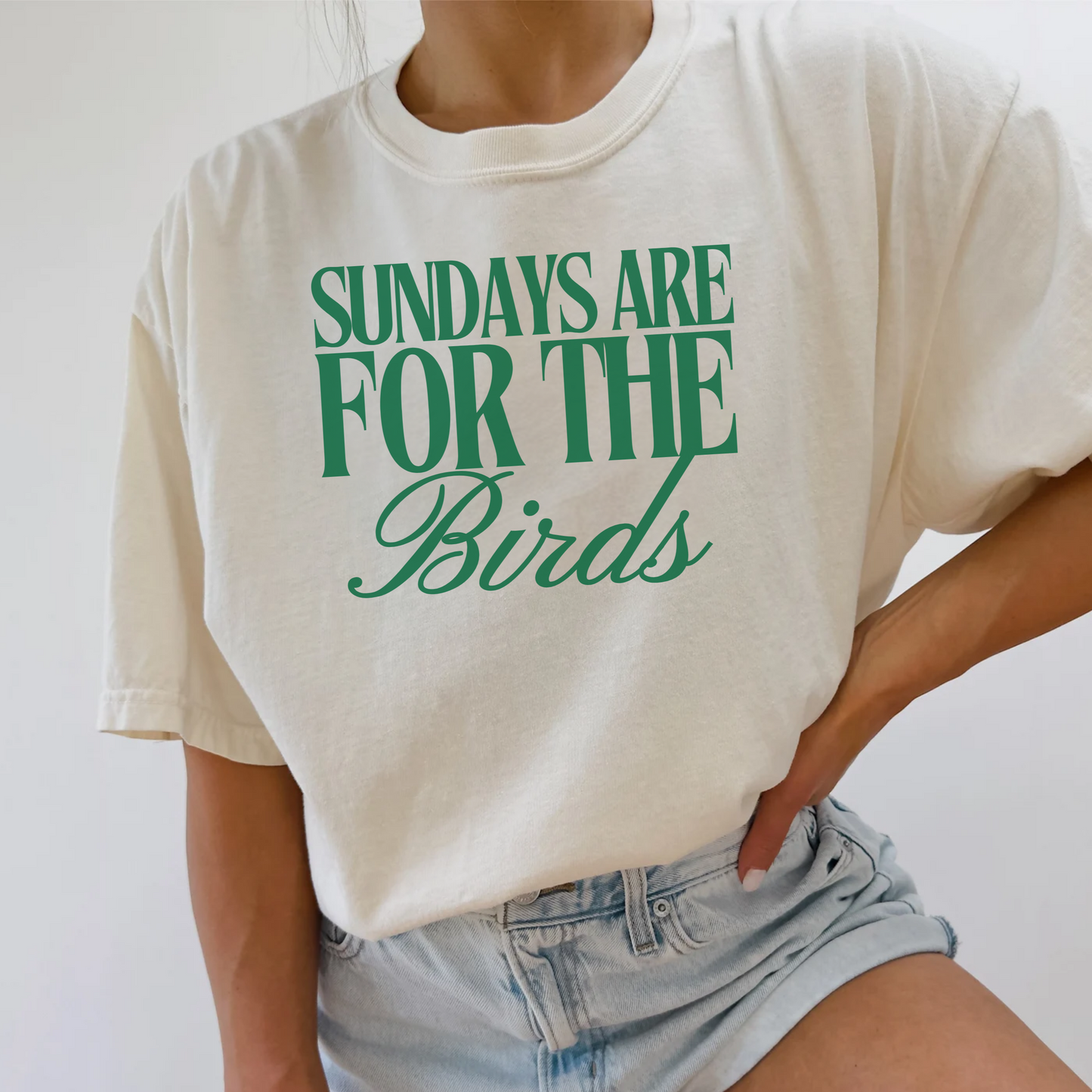 Person wearing a white t-shirt with green text 'Sundays are for the Birds' on a plain background