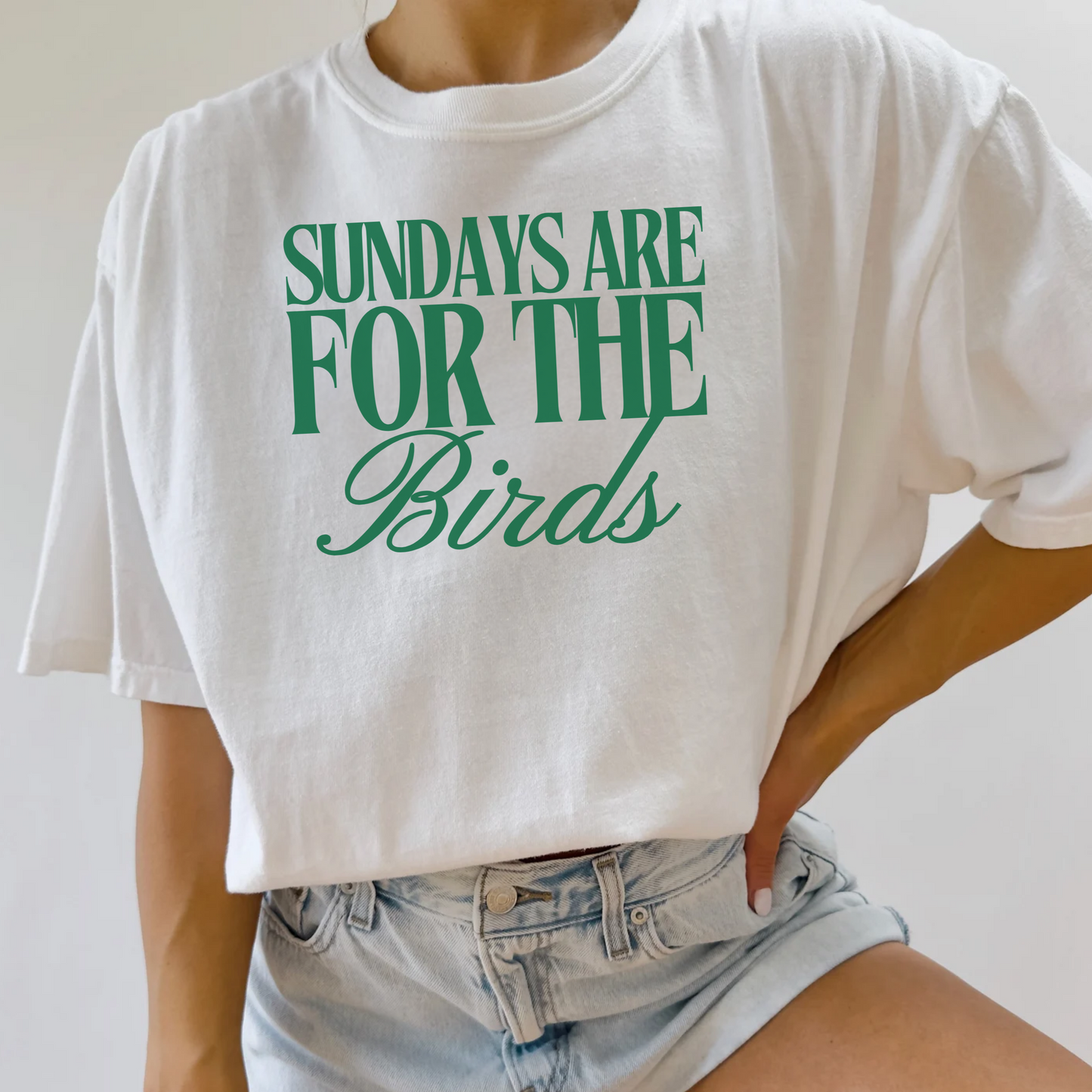White t-shirt with 'Sundays are for the Birds' text worn by a person, on a plain background.