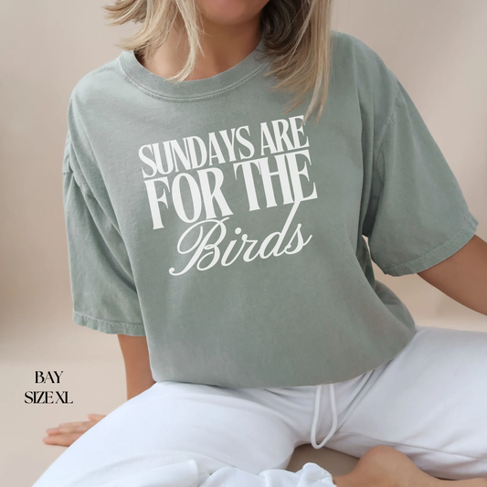 Person wearing a green t-shirt with 'Sundays are for the Birds' text on a beige background