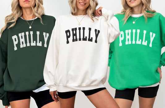Three women wearing sweatshirts with 'PHILLY' printed on them against a white background.