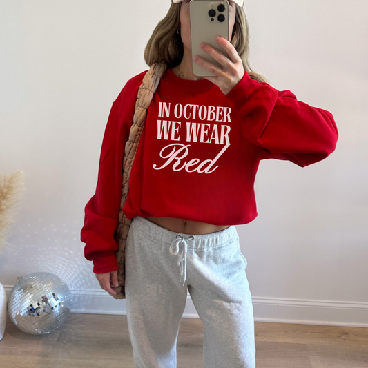 Person wearing a red sweatshirt with 'IN OCTOBER WE WEAR RED' text, taking a mirror selfie.