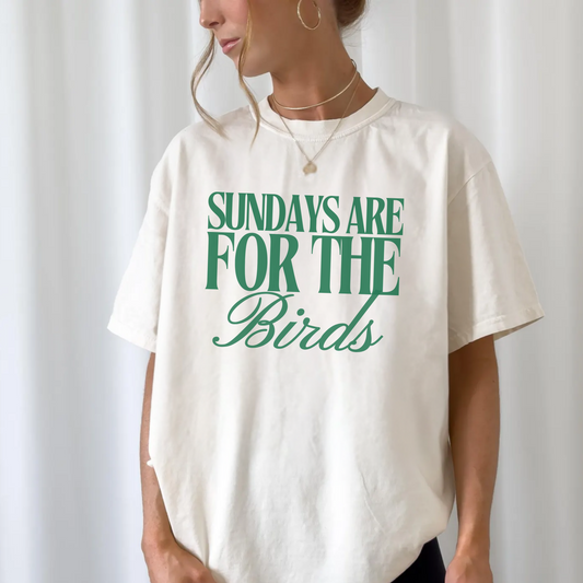 Person wearing a white t-shirt with green text 'Sundays are for the Birds' on a plain background