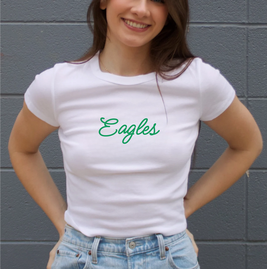 Woman wearing a white t-shirt with 'Eagles' printed on it against a gray wall.